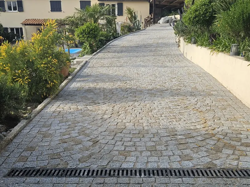 Caniveau à grille intégré dans une allée pavée en pente