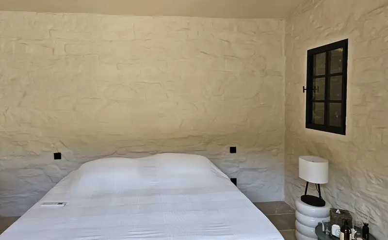 Chambre avec mur en pierre enduit à la chaux et fenêtre en acier noir