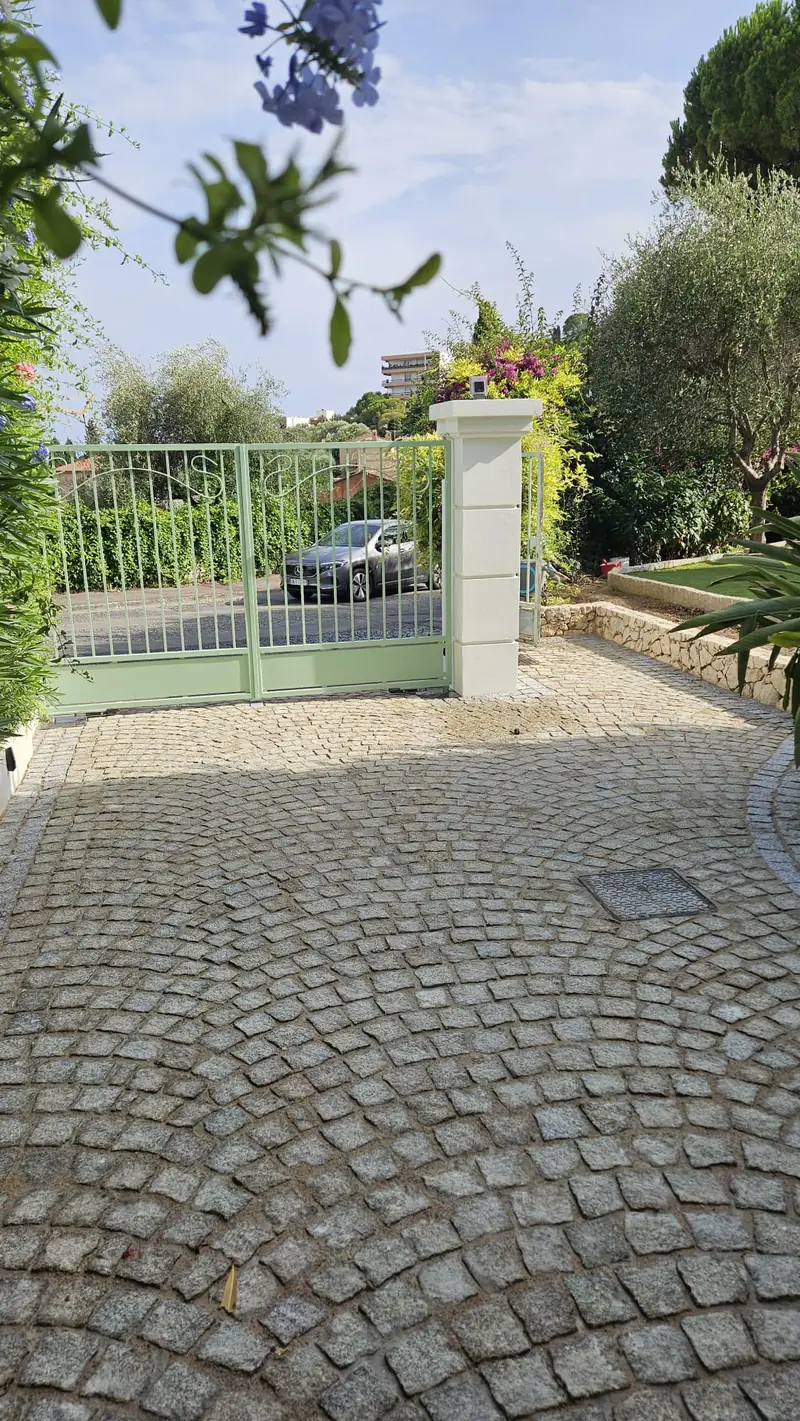 Cour pavée en éventail devant un portail en fer forgé et un pilier maçonné