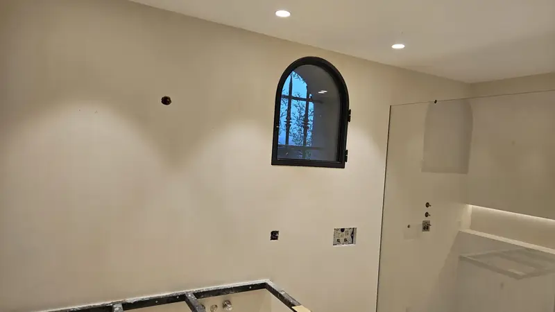 Mur enduit avec fenêtre cintrée en menuiserie noire et spots encastrés