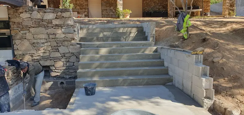 Escalier extérieur en béton coulé en place entre un mur en pierre et un mur en agglos