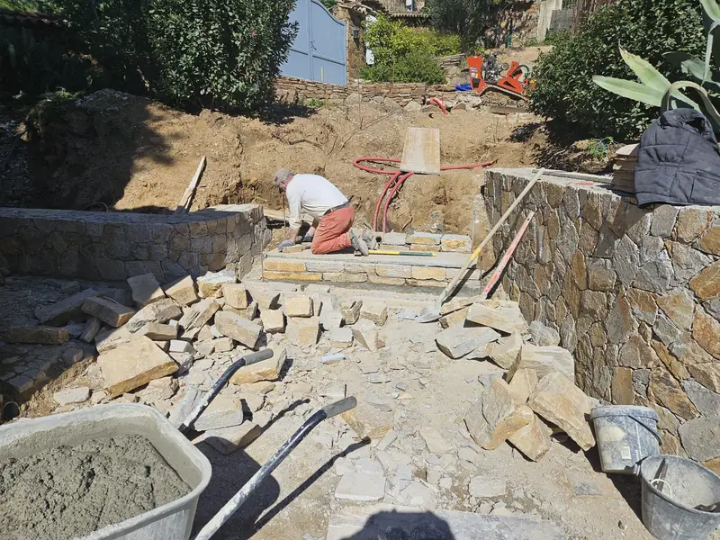 Maçon posant les marches d’un escalier en pierre entre deux murs de soutènement