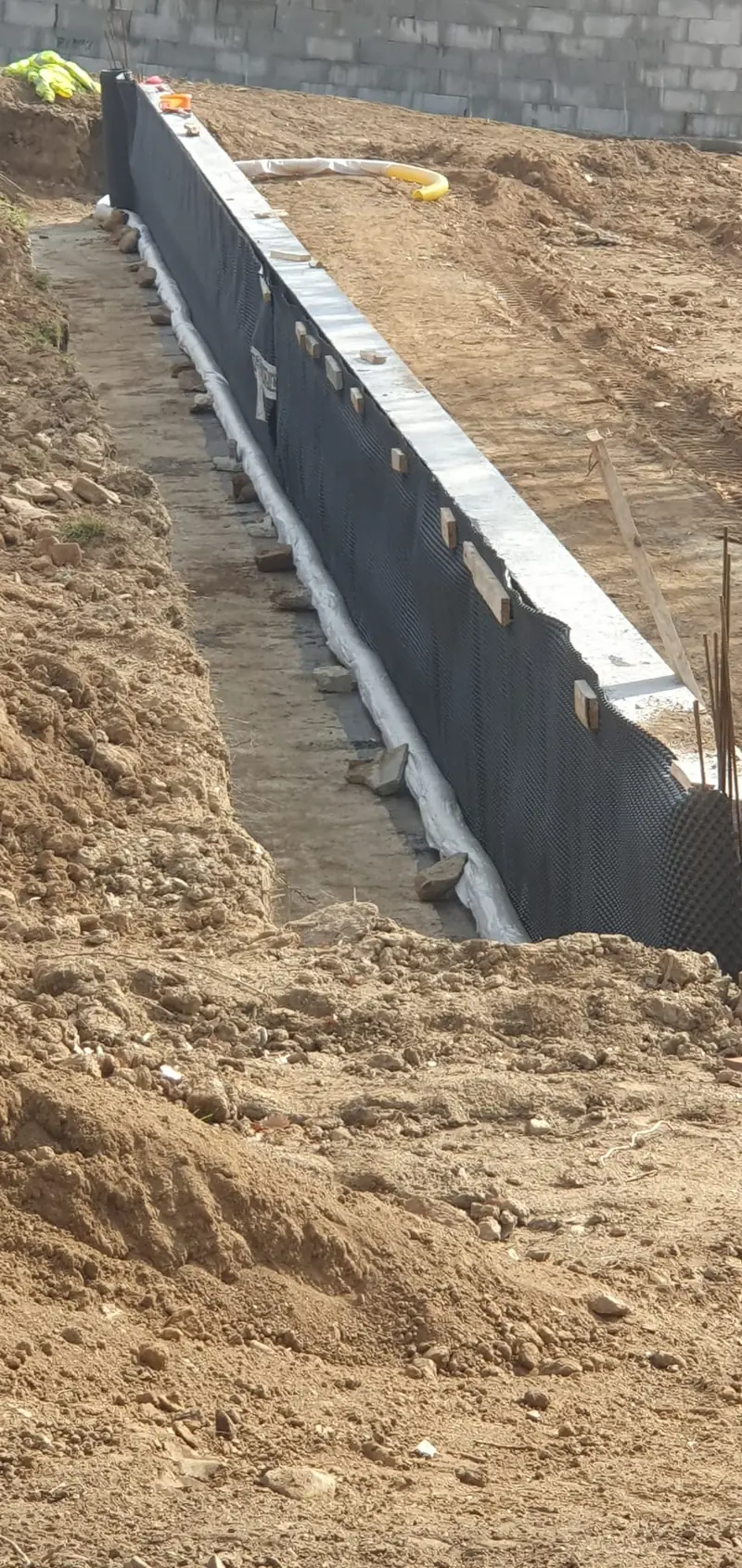Étanchéité noire appliquée sur un mur de soutènement avant remblaiement