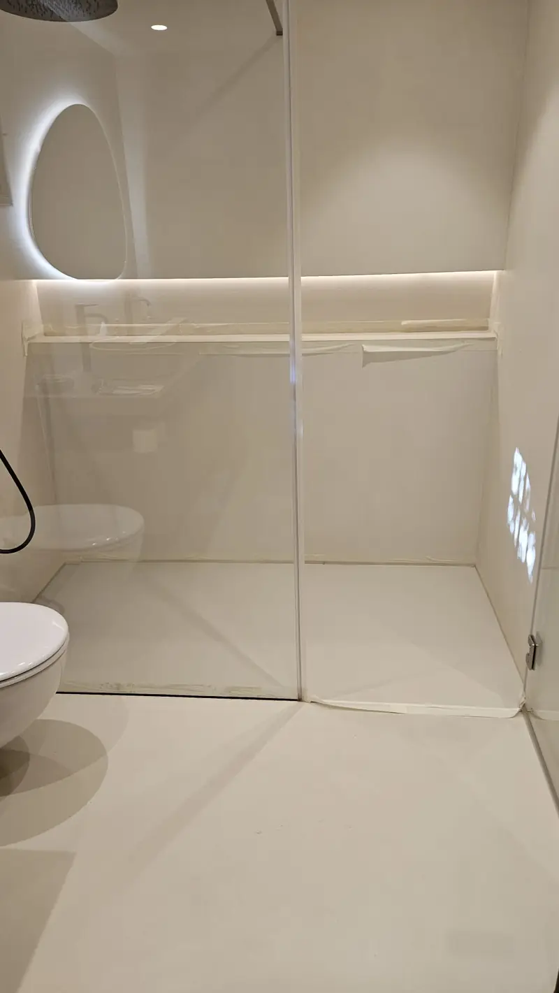 Salle d’eau terminée en béton ciré clair avec miroir rond rétroéclairé
