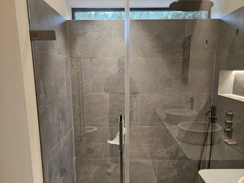 Douche carrelée en grès gris avec paroi vitrée et robinetterie encastrée