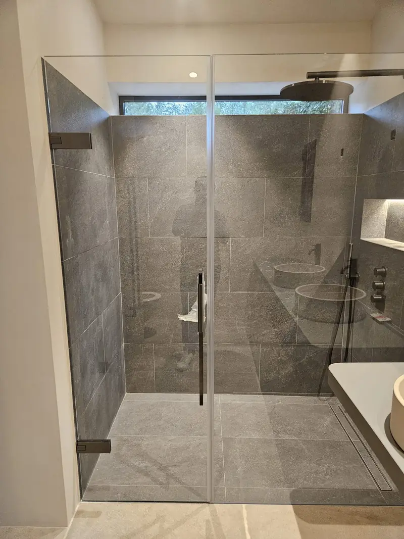 Douche carrelée en grès gris avec paroi vitrée et robinetterie encastrée