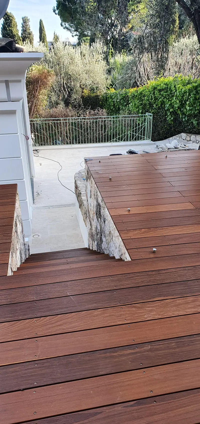 Terrasse bois en encorbellement sur un mur en pierre avec escalier en travertin