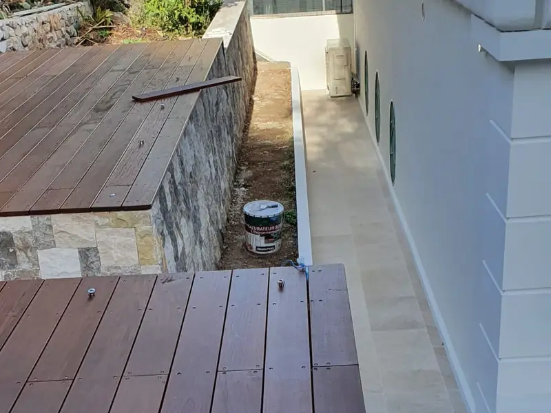 Terrasse bois bordée d’un muret en pierre le long d’une villa